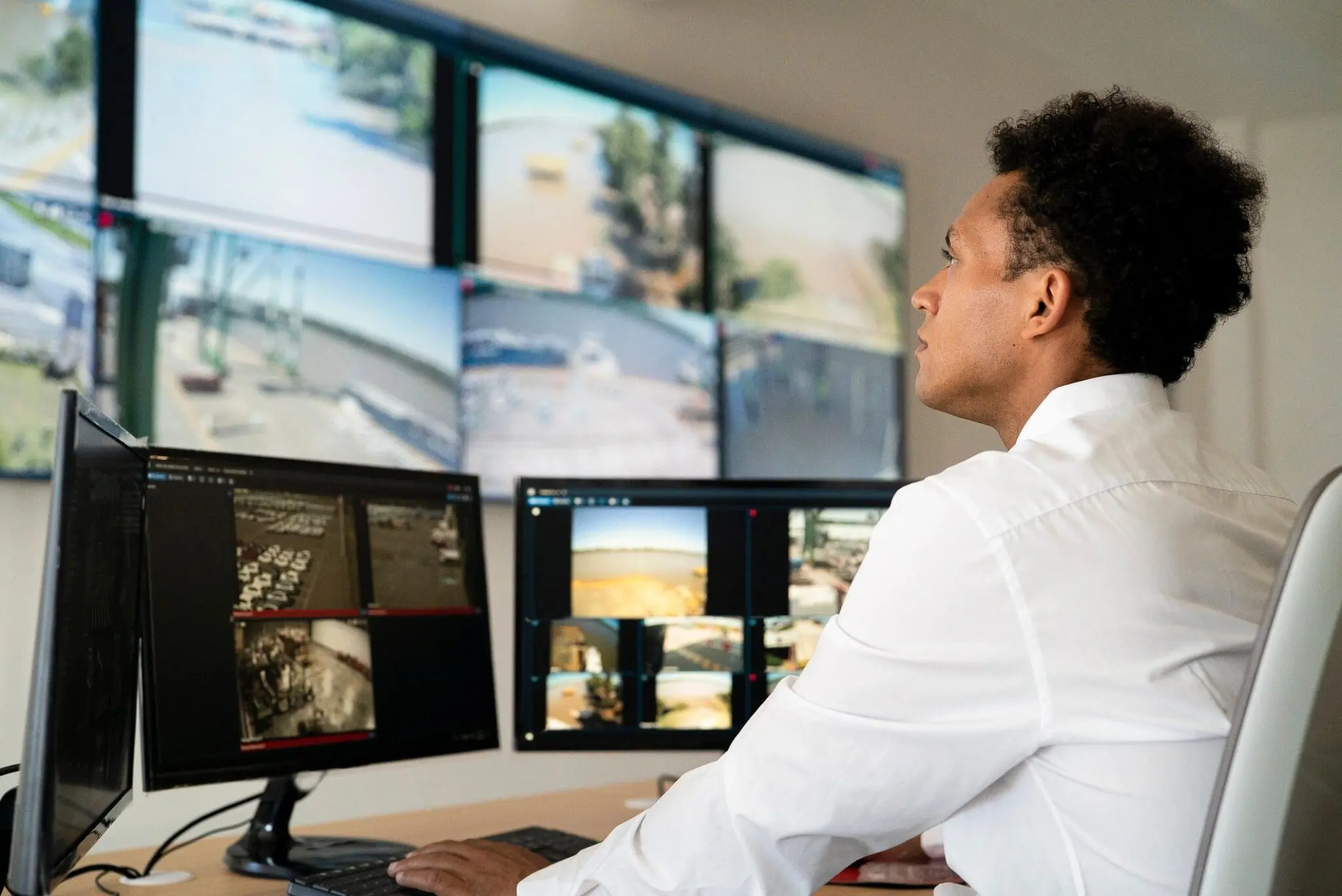 Person monitoring multiple surveillance screens at desk.