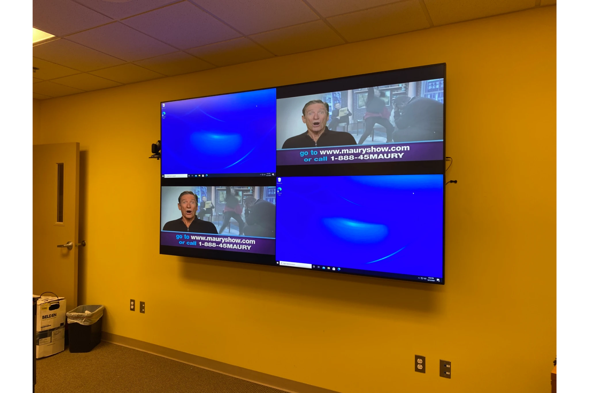 Wall-mounted four-screen display showing TV broadcast
